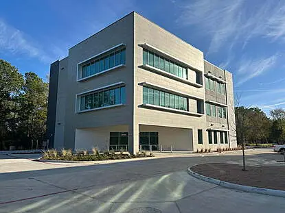 fuel maxx hq Modern three-story office building with large rectangular windows and clean architectural lines, surrounded by trees and a curved driveway under a clear sky.